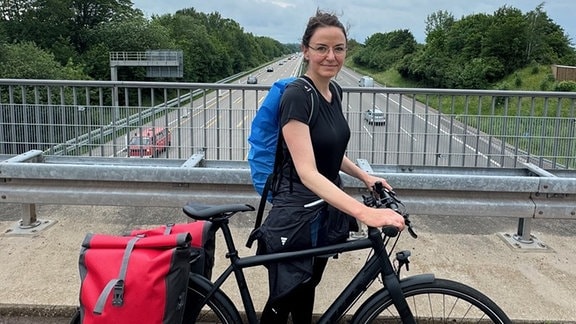 Eine Frau steht mit einerm Fahrrad auf einer Brücke.