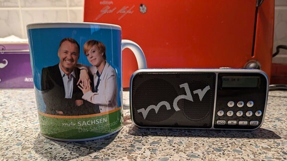 Eine Tasse steht neben einem Taschenradio mit der Aufschrift MDR.