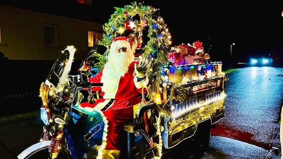 Ein Weihnachtsmann auf einem bunt beleuchteten Elektrodreirad.