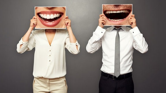 Zwei Personen halten Bilder mit lachenden Mündern vor ihr Gesicht.