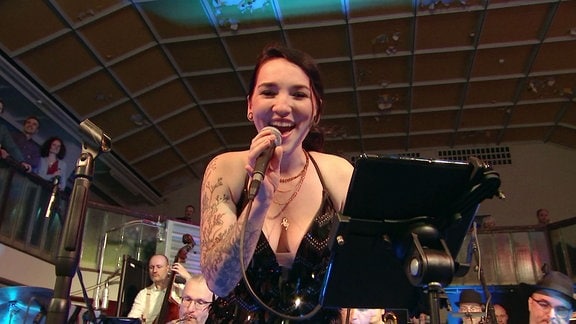 Sängerin schaut singend und lachend in die Kamera.