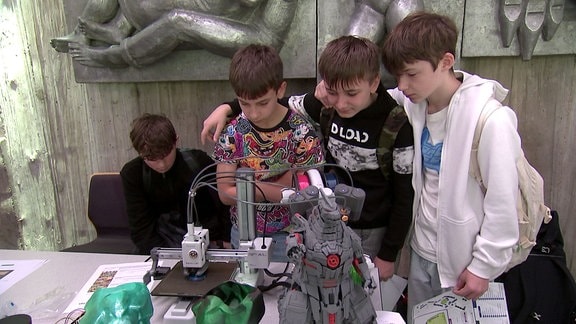 Drei Jungen stehen neben einem 3D-Drucker.
