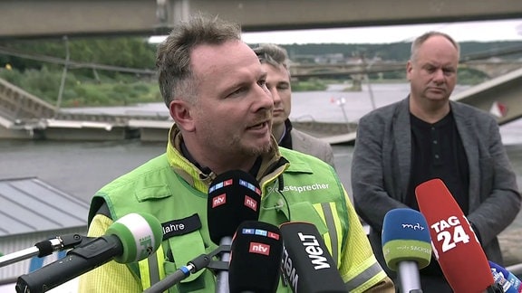 Ansprache zur Presse, im Hintergrund die teileingestürzte Brücke.