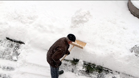 Ein Mann schiebt auf einer Straße Schnee.