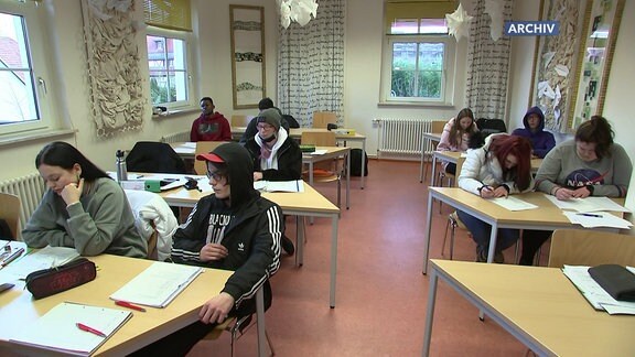 Schüler*innen sitzen in einem Klassenraum an ihren Tischen.