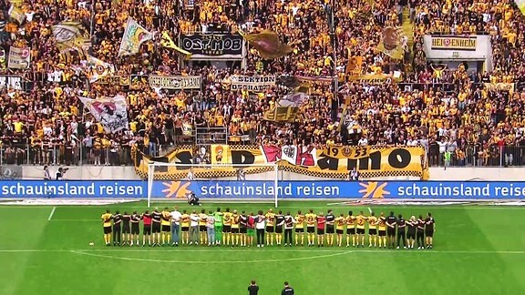 Die Mannschaft von Dynamo Dresden steht in einer Reihe vor der Fankurve.