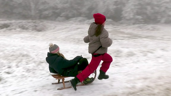 Kinder freuen sich beim Schlittenfahren über den ersten Schnee