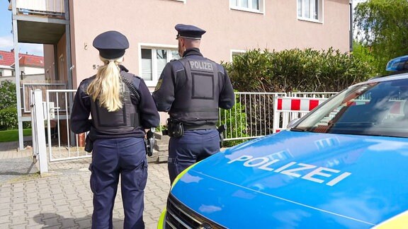 Zwei Polizeibeamte stehen vor einem Wohnhaus