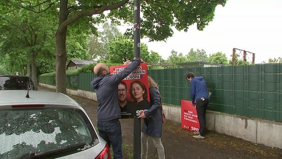 Drei Personen hängen Wahlplakate der SPD auf.