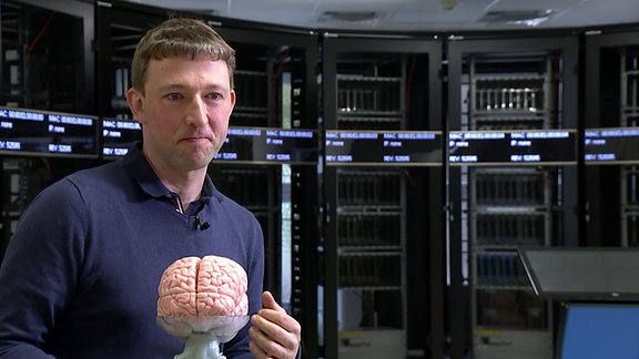 Johannes Partzsch (TU Dresden / Fakultät Elektrotechnik) steht mit einem Gehirn-Modell im Computerraum