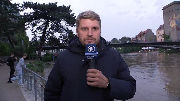 Der Reporter steht vor einem Fluss