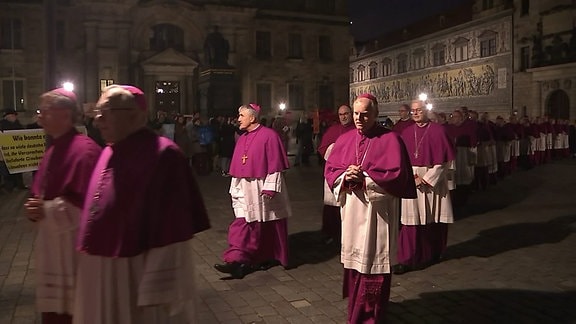 Viele Geistliche laufen abends in einer Reihe über einen Hof.