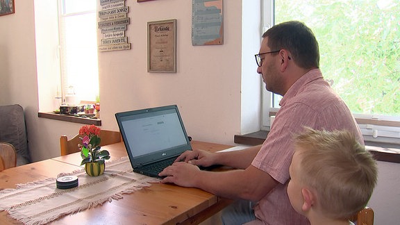Ein kleiner Junge und ein Mann sitzen vor einem Laptop