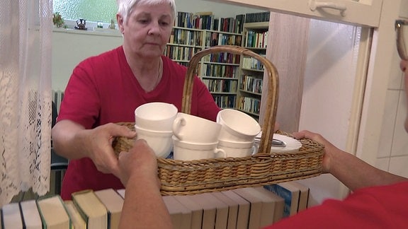 Zwei Frauen in roten Shirts übergeben Kaffeegeschirr auf einem Tablett.