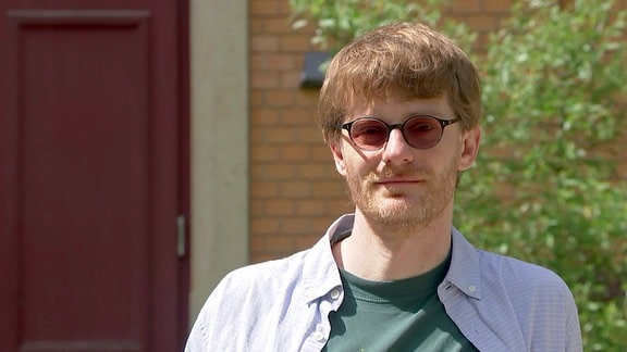 Ein junger Mann mit Brille vor seiner ehemaligen Schule