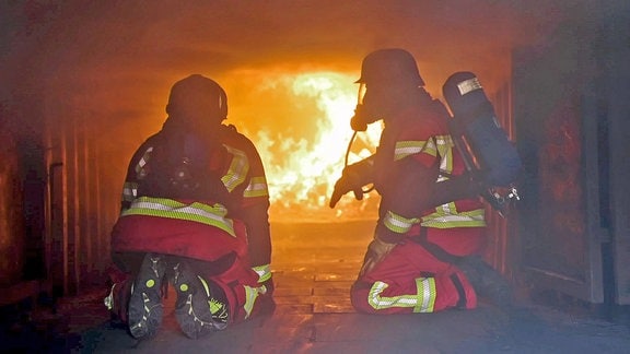 Zwei Feuerwehrleute in Schutzanzügen vor einem Feuer