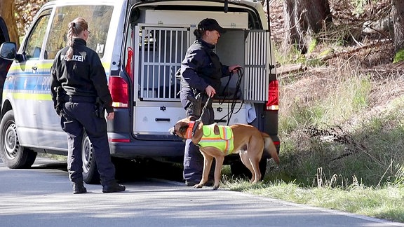 Polizeikräfte mit Spürhund vor einem Dienstfahrzeug