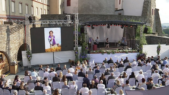 Gäste einer öffentlich Trauerfeier verfolgen die Veranstaltung auf der Bühne