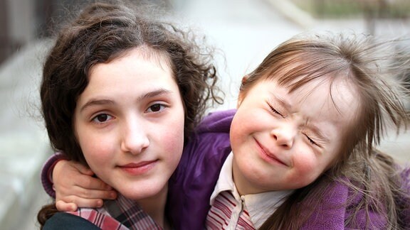 Zwei Mädchen umarmen sich, das kleinere Mädchen hat das Down-Syndrom