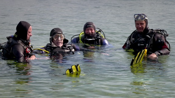 Vier Menschen in Tauchausrüstung schwimmen an einer Wasseroberfläche.