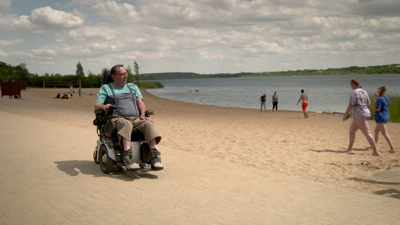 Ein Mann sitzt in einem Rollstuhl an einem See.