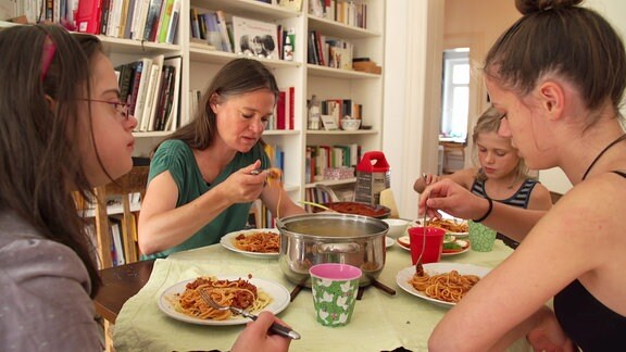 Eine Frau und drei Mädchen sitzen an einem Tisch und essen.