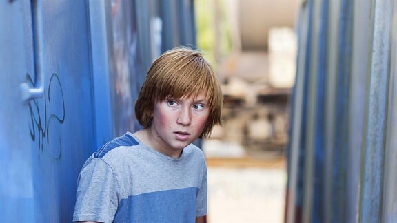 Ein Junge steht zwischen zwei Containern.