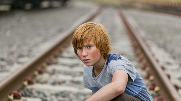 Ein Junge hockt auf einem Gleis.