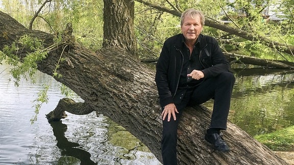 Ein älterer Mann sitzt auf einem Baum, der über einen Fluss reicht.