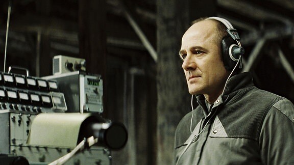 Ein Mann mit Kopfhörern sitzt an einem technischen Apparat.
