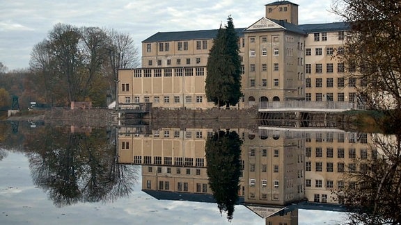 Ein großes Gebäude steht am Rande eines Gewässers. Zu sehen ist die Sachsenburg, ein Konzentrationslager, das von den Nationalsozialisten eingerichtet wurde.