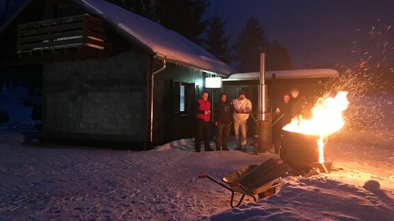 Eine Gruppe Angler wärmt sich vor einer brennenden Feuertonne auf. 