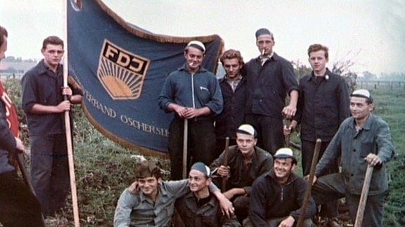 Jugendliche Arbeiter neben einer FDJ-Fahne