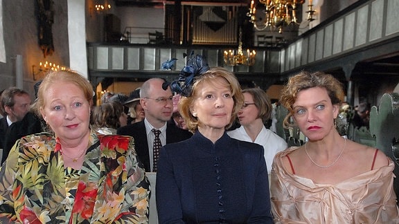  Luise (Christiane Hörbiger, Mitte), ihre Tochter Charlotte (Margarita Broich, re.) und ihre Haushälterin Rita (Ulrike Bliefert) in einemgefüllten Saal stehend .