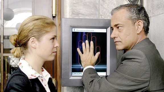 Bankdirektor Conrad (Rolf Kanies, rechts) deaktiviert das Sicherheitssystem der Kommanditbank. Tochter Sandra (Luise Helm, links) beobachtet ihn skeptisch.