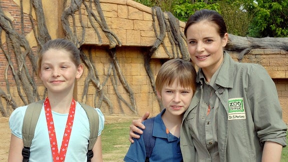 Susanne Mertens (Elisabeth Lanz, r.), ihr Sohn Jonas (Ludwig Zimmeck, M.) und dessen Freundin Rebecca (Elisabeth Böhm, l.) freuen sich darüber, dass das kambodschanische Mädchen aus dem Rollstuhl aufgestanden ist.