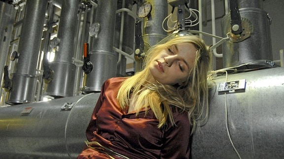 Anna Stein (Annika Blendl)sitzt gefesselt und bewusstlos vor einem Rohr.