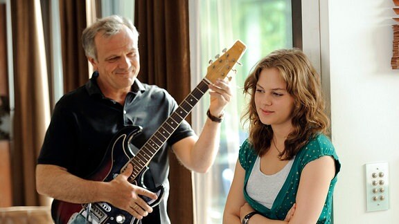 Clara (Alicia von Rittbergsteht neben ihrem  Vater Erik (Bernhard Schütz), der Gitarre spielt.