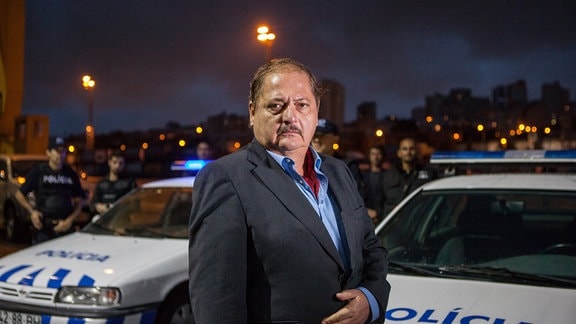 Eduardo Silva (Jürgen Tarrach) vor Polzeifahrzeugen; das nächtliche Lissabon im Hintergrund,