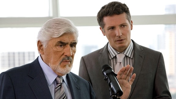 Konrad Hansen (Mario Adorf, li.) und sein Sohn Lars (Max Urlacher) vor einem Mikrofon.