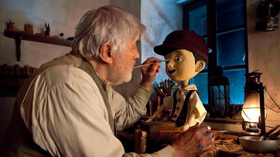Geppetto (Mario Adorf) bemalt die Augen seiner Puppe.