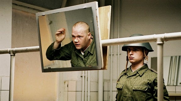 Henrik (Kim Frank) und Krüger (Oliver Bröcker, im Spiegel) üben den ausdruckslosen Blick und freunden sich trotz ihrer Gegensätzlichkeit miteinander an.