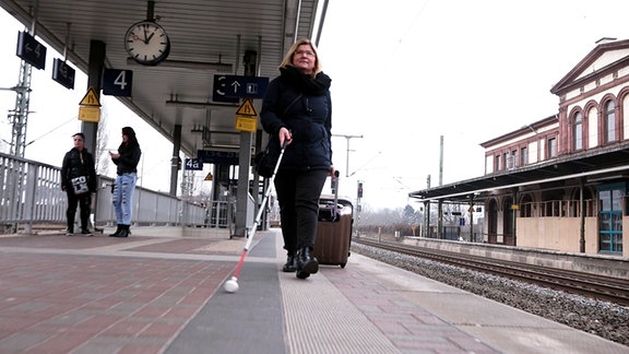 Eine Frau mit Blindenstock bewegt sich au einem Bahnsteig.