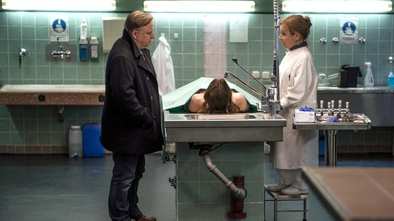 Silke Haller alias "Alberich" (ChrisTine Urspruch) und Frank Thiel (Axel Prahl) neben einem Obduktionstisch auf dem eine Leiche liegt.