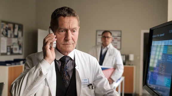 Hans-Peter Brenner (Michael Trischan, hinten) wundert sich, als er Dr. Kaminski (Udo Schenk, vorn) im Ärztezimmer aufgebracht russisch reden hört.