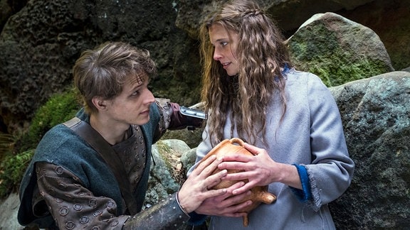 Jolanthe (Svenja Jung) und Veit von Hammerlitz (Merlin Rose) stehen auf einer Waldlichtung dicht bei einander, umfassen den magischen Topf und blicken sich tief in die Augen.