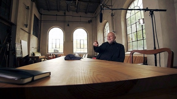 Thomas Thieme sitzt an einem großen Tisch