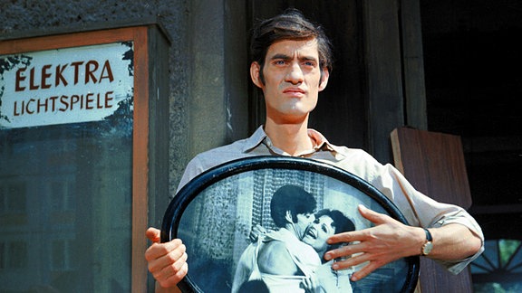 Paul (Winfried Glatzeder) steht mit einem Erinnerungsfoto von ihm und Paula (Angelica Domröse) vor Paulas Haus.