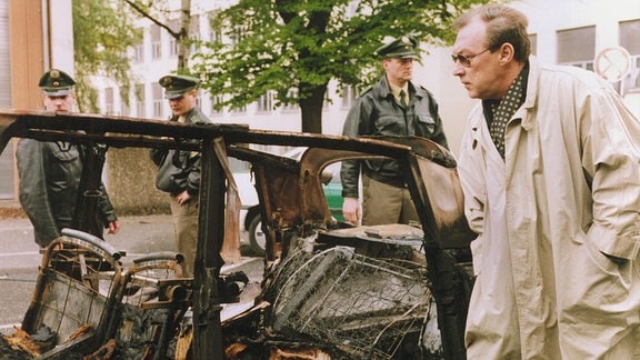 Kommissar Schmücke (Jaecki Schwarz) untersucht das ausgebrannte Auto.