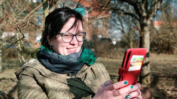 Louisa bedient ein Smartphone, Im Hintergrund sind Bäume zu sehen.